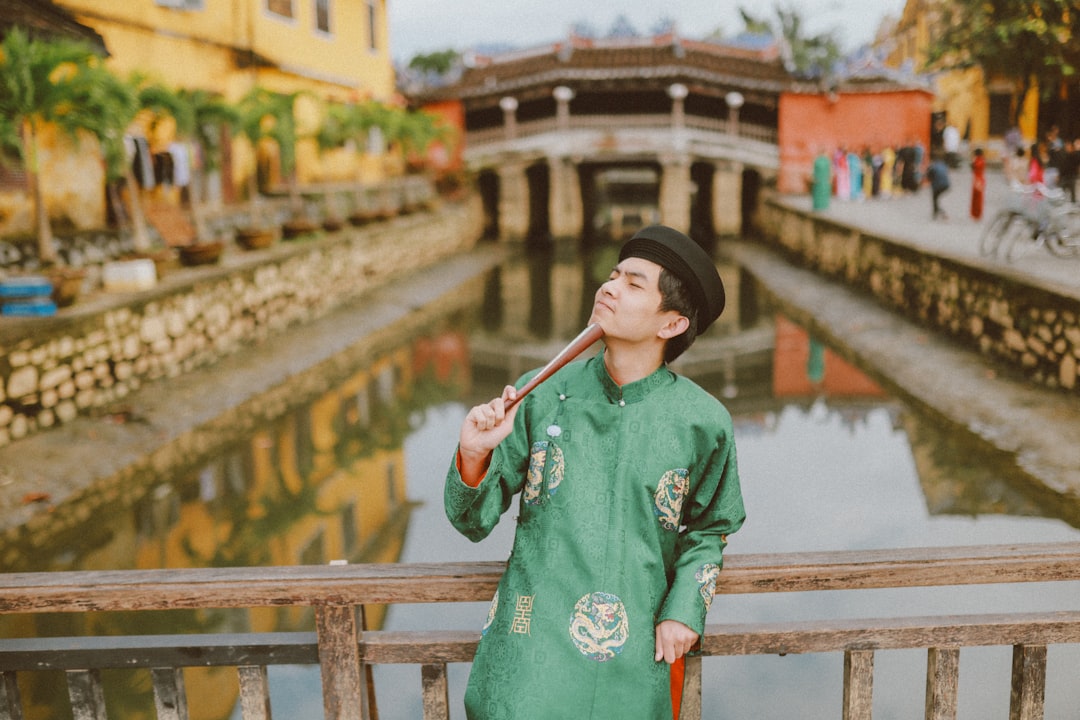 Man in green traditional clothing stands on bridge